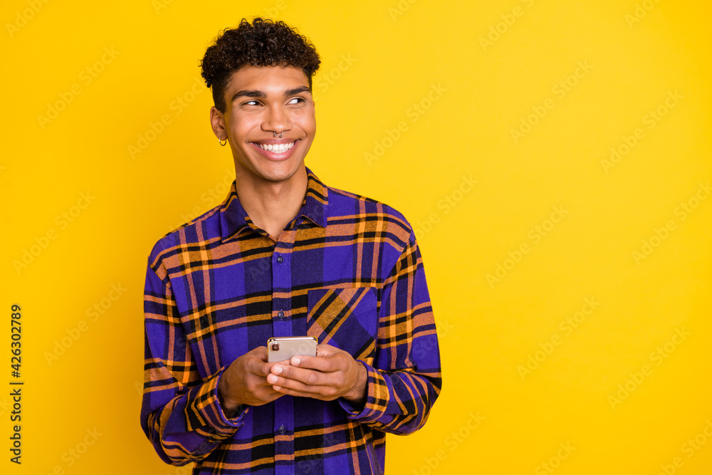 Photo portrait of man browsing internet mobile phone looking empty space wearing checkered outfit isolated on vivid yellow color background Photo portrait of man browsing internet mobile phone looking empty space wearing checkered outfit isolated on vivid yellow color background