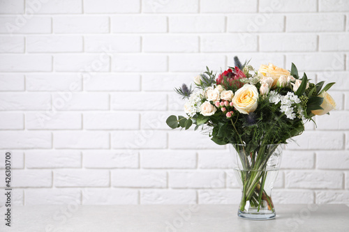 Beautiful bouquet with roses on grey table against white brick wall, space for text