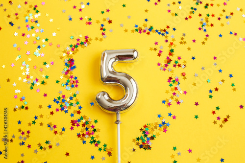 five years birthday party. number five with multicolored confetti in the form of stars on a yellow background