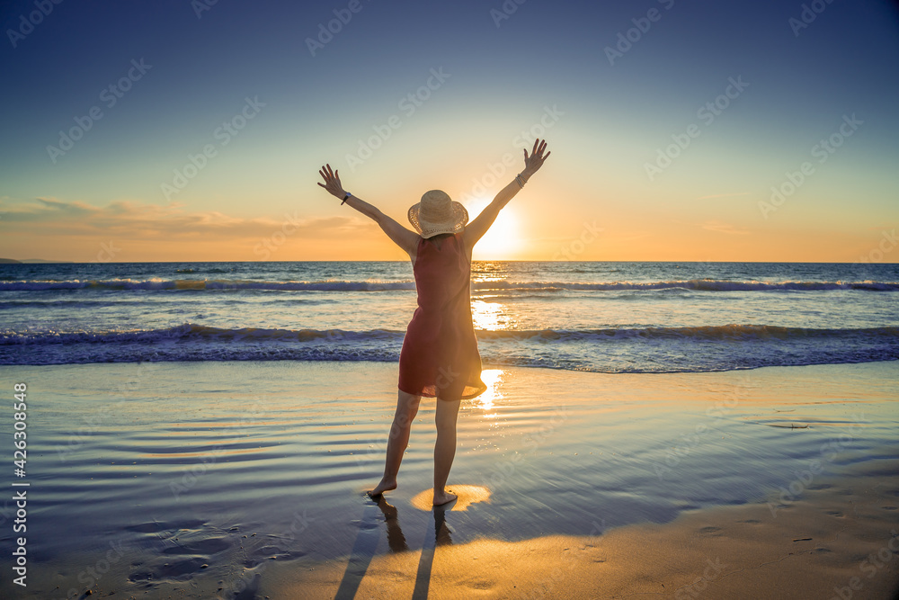 Woman in red with arms outstretched by the sea at sunrise enjoying freedom and life