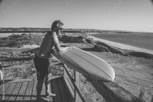 Portrait of mature senior Surfer looking at the ocean with vintage surfboard on an empty beach