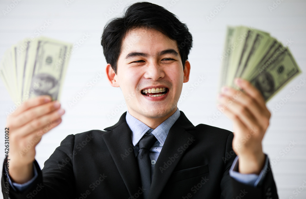 Closeup portrait shot of Asian young handsome black short hair successful rich businessman wears formal suit and necktie laugh and satisfy with full US dollar hundred banknotes currency in hands Closeup portrait shot of Asian young handsome black short hair successful rich businessman wears formal suit and necktie laugh and satisfy with full US dollar hundred banknotes currency in hands