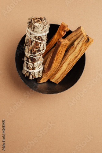 Set of incense for fumigation. White sage sprigs and Palo Santo sticks tied in bunch in metal bowl. View from above. Organic holy tree incense from Latin America. Close-up color photo.