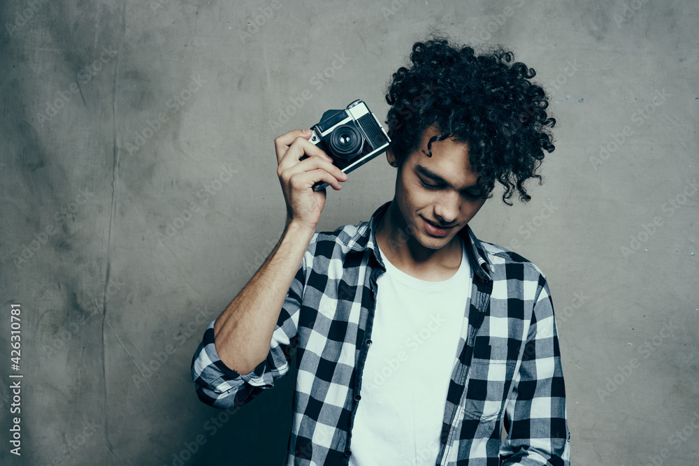 Fototapeta premium young man with a camera in hand and in a plaid t-shirt on a gray background indoors photographer