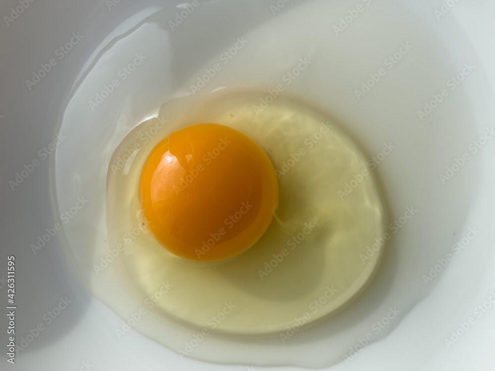 One bright yellow raw chicken egg in a white bowl. One bright yellow raw chicken egg in a white bowl.