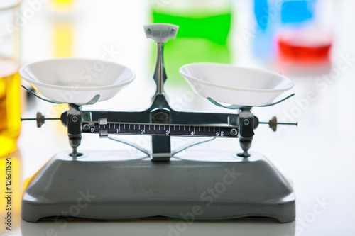 Closeup shot of empty black and gray metal weight scales with white trays placed on table in laboratory in blurred colorful reagent in beakers and lab equipment background