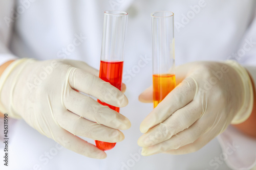 Closeup shot of liquid in glass in test tube holded by scientist in white lab coat and rubber gloves hands.