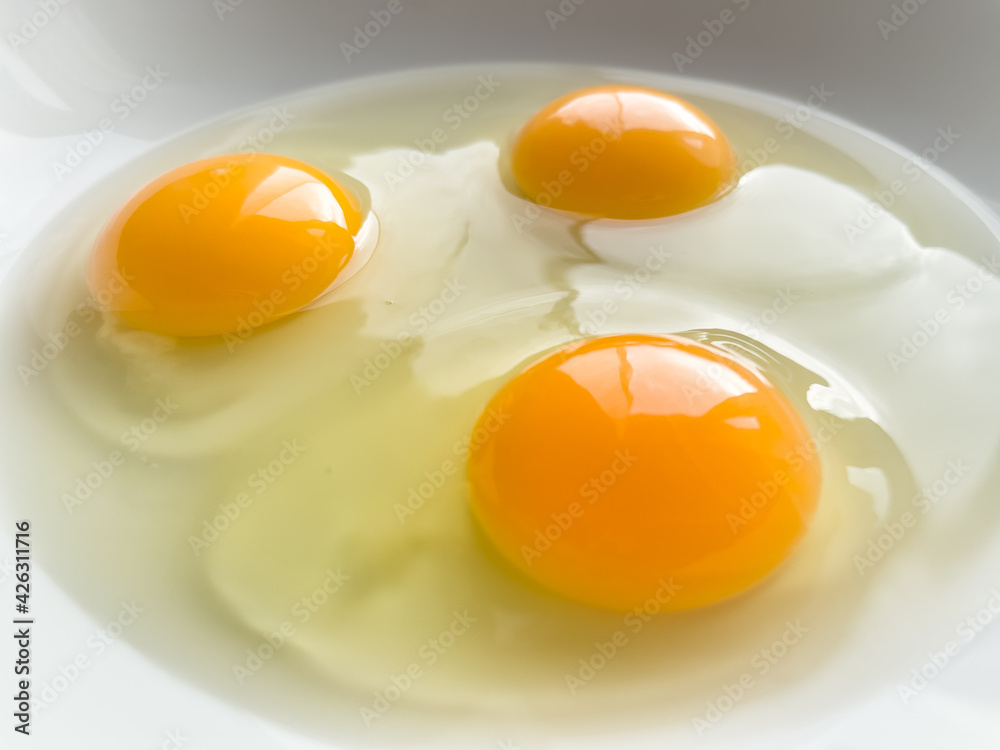 Three bright yellow raw chicken eggs in a white bowl. Three bright yellow raw chicken eggs in a white bowl.