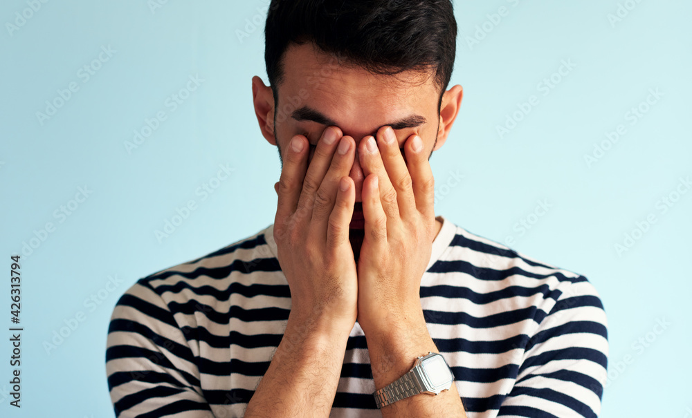 Portrait of an upset young man cover his eyes with hands, posing against white blue wall. Sad male feels worried. Portrait of an upset young man cover his eyes with hands, posing against white blue wall. Sad male feels worried.