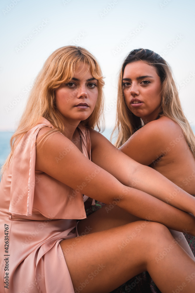 Portrait of a couple of Caucasian girls having fun sitting in very nice dresses enjoying the summer by the sea Portrait of a couple of Caucasian girls having fun sitting in very nice dresses enjoying the summer by the sea