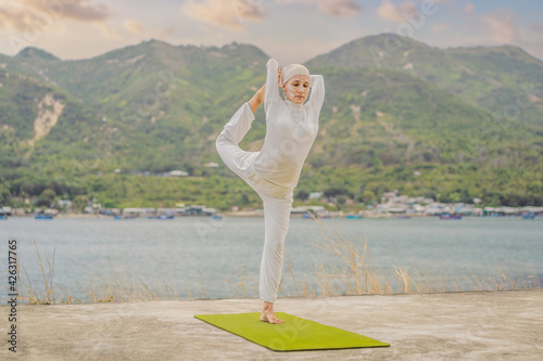 Kundalini yoga woman in white clothes and turban practices yoga kundalini on the background of the sea, mountains and sunset. Fighting face painting of the Indians shows her inner world. Visual photo