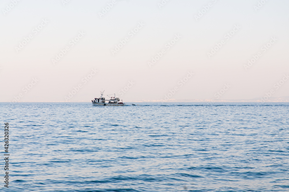 lonesome fisher boat on calm sea against a misty and bright horizon in the mediterranean sea