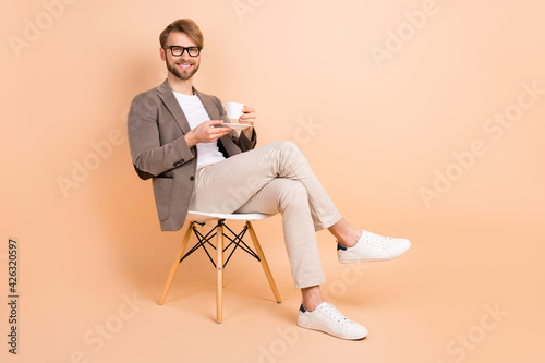 Full size photo of happy handsome attractive charismatic man in glasses relaxing drink tea isolated on beige color background