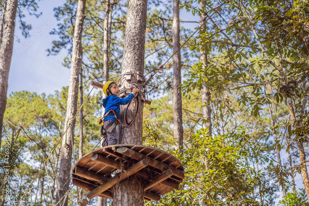 Happy child in a helmet, healthy teenager school boy enjoying activity in a climbing adventure park on a summer day Happy child in a helmet, healthy teenager school boy enjoying activity in a climbing adventure park on a summer day