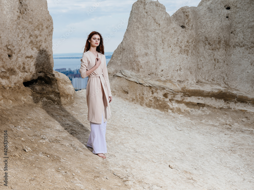 romantic traveler in light clothes on the sand near high rocks
