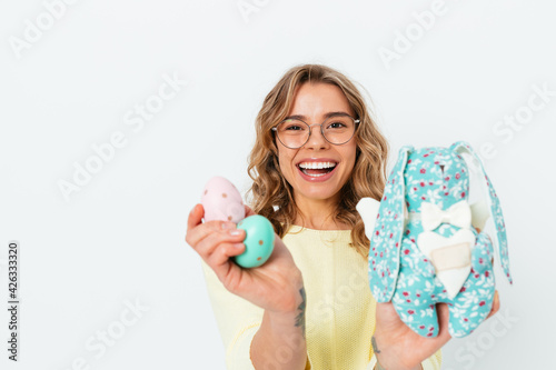 Happy joyful young woman celebrating Easter holding toy bunny and colored eggs