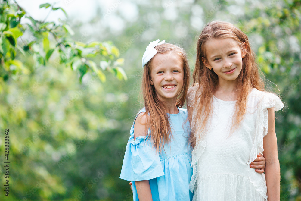 Adorable little girls in blooming apple tree garden on spring day Adorable little girls in blooming apple tree garden on spring day