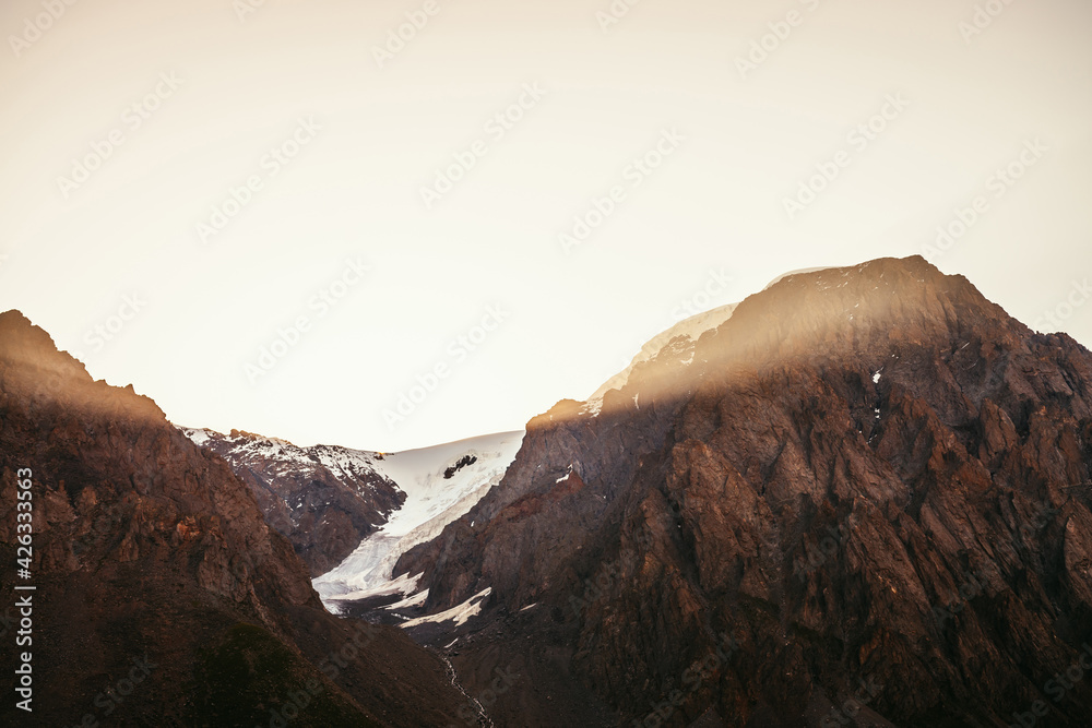 Golden rays of rising sun on high snowy mountain top with glacier. Beautiful morning landscape with gold sunlight in big mountains. Minimalist colorful scenery with golden sunbeams. Sunny minimalism.