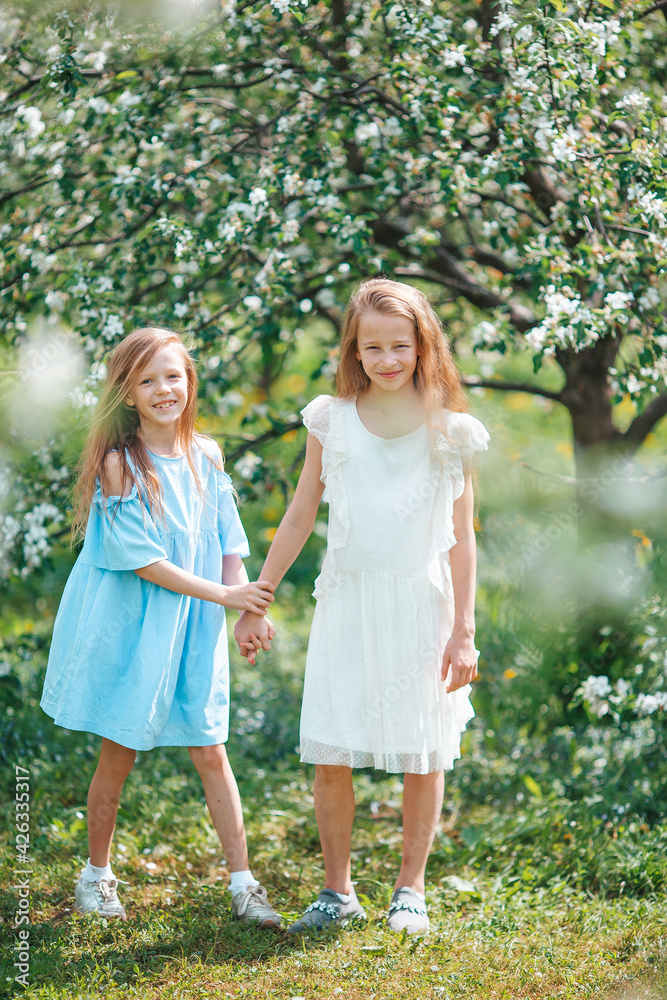 Adorable little girls in blooming apple tree garden on spring day