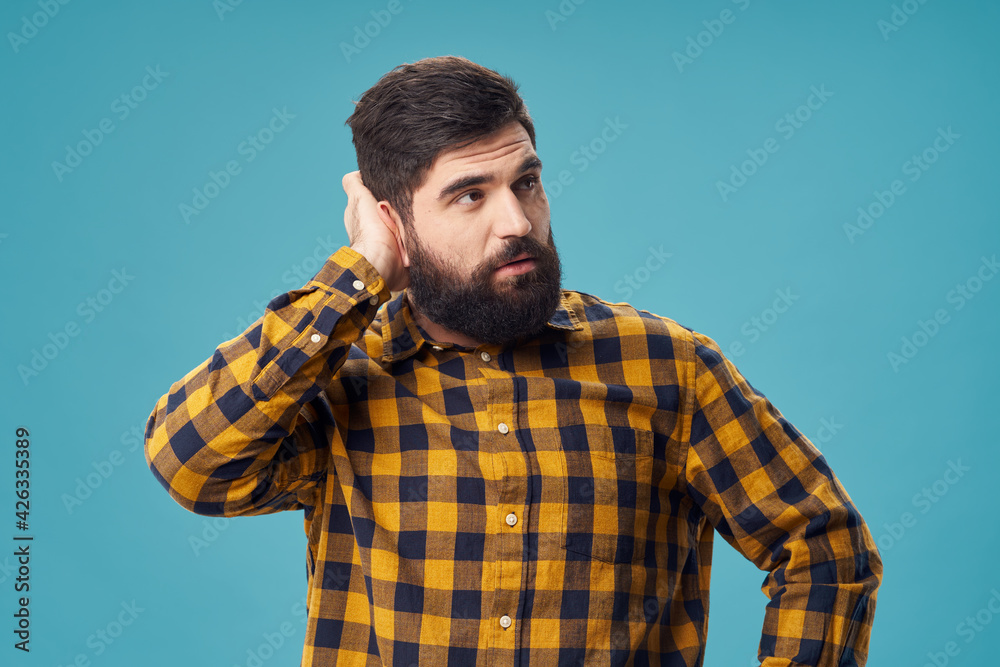handsome man with a beard and in a plaid shirt touches his head with his hand handsome man with a beard and in a plaid shirt touches his head with his hand