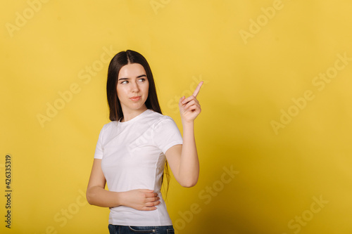 Portrait of attractive young woman pointing fingers away at copy space isolated over yellow background