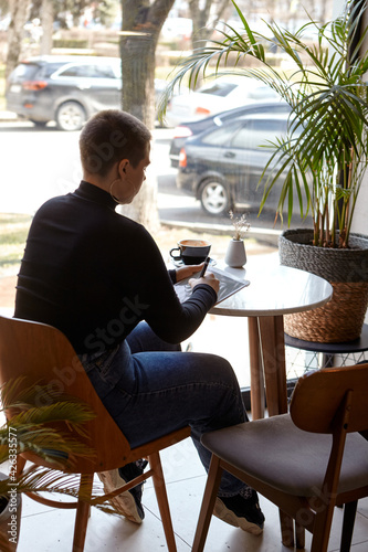 Young girl with short hair and nose piercing sits in a cafe and work at a tablet. The concept of freelancing and remote work.