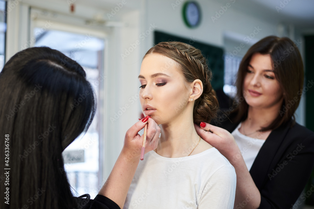 Getting ready for party. Young pretty girl sitting in beauty salon while hairdresser and make-up artist making her look beautiful. Professional work process in studio. Love yourself. Bride's morning. Getting ready for party. Young pretty girl sitting in beauty salon while hairdresser and make-up artist making her look beautiful. Professional work process in studio. Love yourself. Bride's morning.