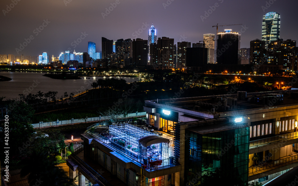 Haikou cityscape with rooftop terrace and view on the coastal city bay and skyline illuminated at night Haikou Hainan China Haikou cityscape with rooftop terrace and view on the coastal city bay and skyline illuminated at night Haikou Hainan China