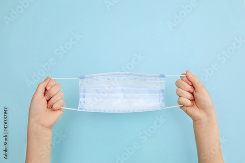 Medical mask in the hands of a child, protective mask on a blue background. A disposable surgical face mask covers the mouth and nose. Healthcare and medical concept.
