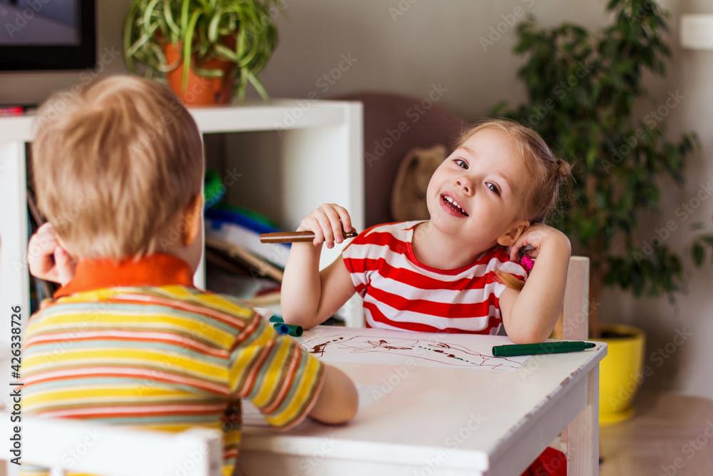Little smiling girl and boy children sits at the table and draws with felt-tip pens, happy childhood Little smiling girl and boy children sits at the table and draws with felt-tip pens, happy childhood