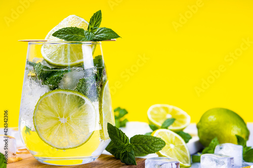Refreshing mojito with lime, mint and ice in a glass on a summer yellow background, free space for text. Cold summer cocktail © Kseniya