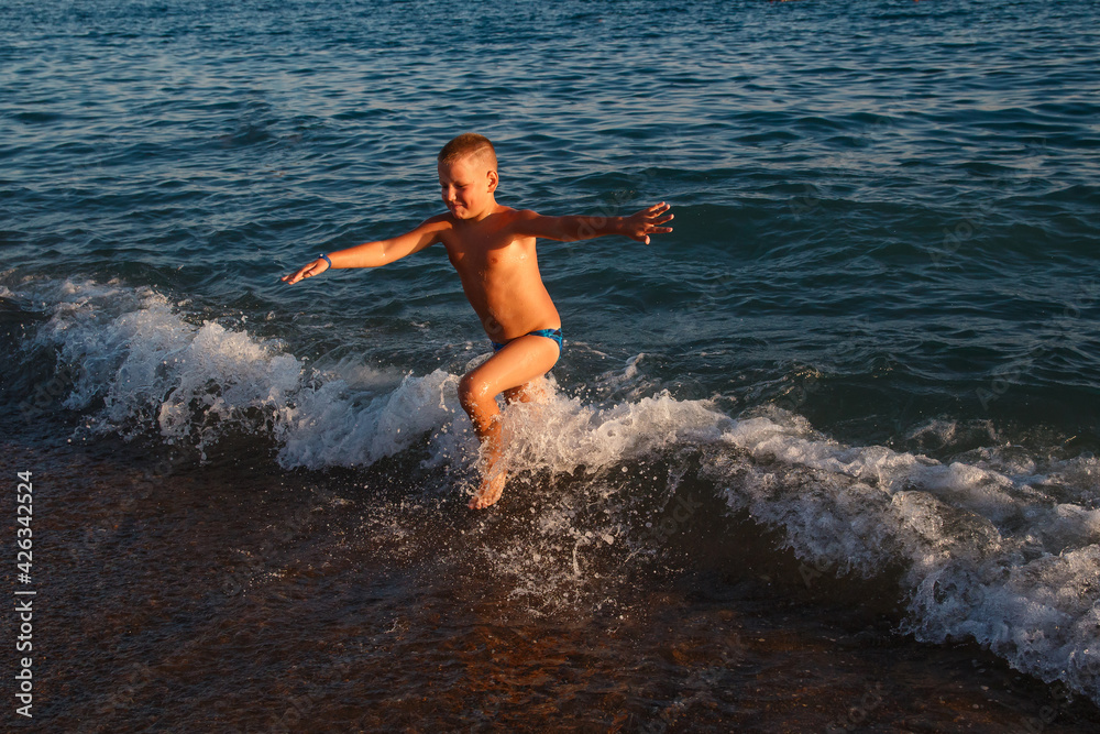 Nine-year-old tanned fat boy runs across the sea in summer