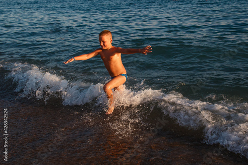 Nine-year-old tanned fat boy runs across the sea in summer