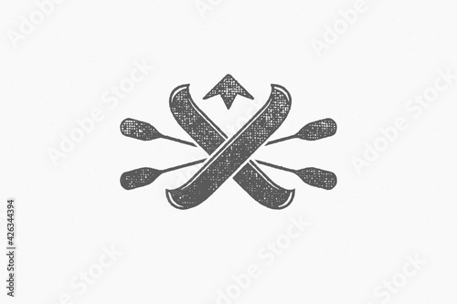 Black logo of oars and kayaks crossed against mountain peak silhouette hand drawn stamp effect vector illustration.