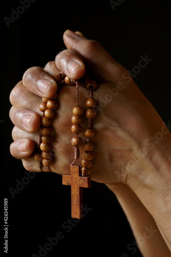 Praying hands of Indian Catholic woman with wooden rosary isolated on a black background.