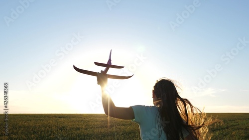 Happy girl runs with toy airplane across field in rays of sunset. Childrens play in toy airplane. Teenager dreams of flying and becoming pilot. Girl wants to become pilot and an astronaut. Slow motion