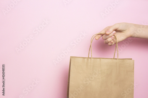 Girl holding in hand beige craft paper bag for shopping on pink background. Shopping concept