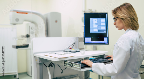 Cute professional woman doctor is working with modern Mammography X-Ray System Machine in a hospital or private clinic. Cancer and disease female treatment concept