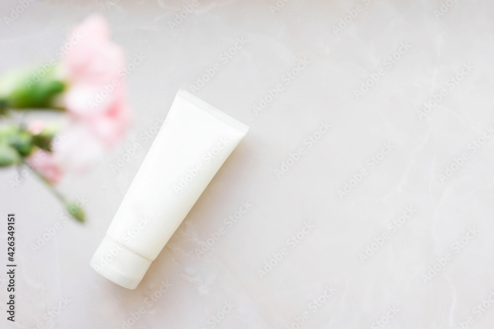 white cosmetic tube with face cream, body lotion or cleanser on a light background with pink flowers. Sensitive skin care concept. Copy space white cosmetic tube with face cream, body lotion or cleanser on a light background with pink flowers. Sensitive skin care concept. Copy space