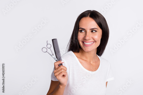 Photo of nice optimistic brunette lady with brush scissors look empty space wear white t-shirt isolated on grey color background