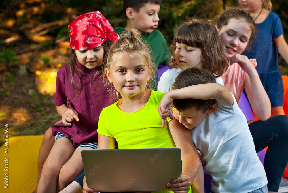 Children play in nature with a laptop. Boys and girls are resting in a tent camp. Children sit on a purple inflatable sofa in summer. Children play in nature with a laptop. Boys and girls are resting in a tent camp. Children sit on a purple inflatable sofa in summer.