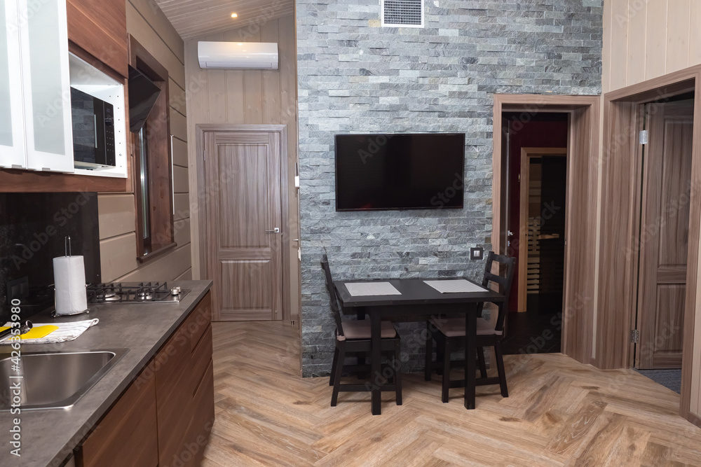 Dining room with TV above the dining table. Interior of a modern kitchen. Kitchen in brown tones with a wall imitating a brick. Interior of the cottage. Guest house from the inside. Dining room with TV above the dining table. Interior of a modern kitchen. Kitchen in brown tones with a wall imitating a brick. Interior of the cottage. Guest house from the inside.
