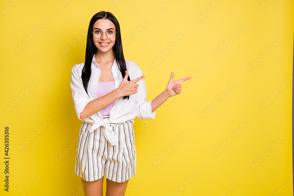 Photo of charming positive lady point index fingers empty space smile isolated on yellow color background Photo of charming positive lady point index fingers empty space smile isolated on yellow color background