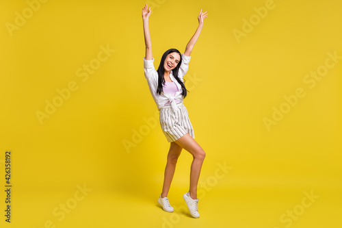 Full size photo of young pretty excited smiling positive girl dancing raise fists up isolated on yellow color background