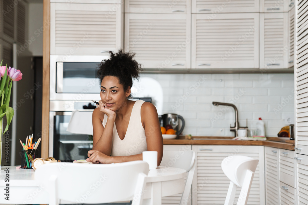 Black woman working with papers while sitting at table in home kitchen Black woman working with papers while sitting at table in home kitchen