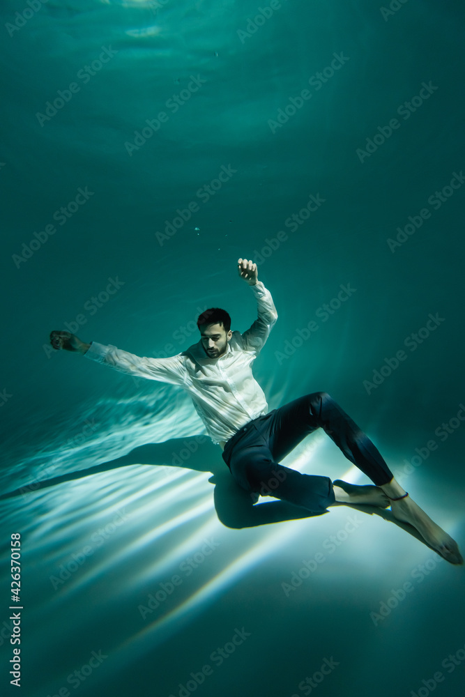 Arabian man in formal wear sitting on bottom of swimming pool Arabian man in formal wear sitting on bottom of swimming pool