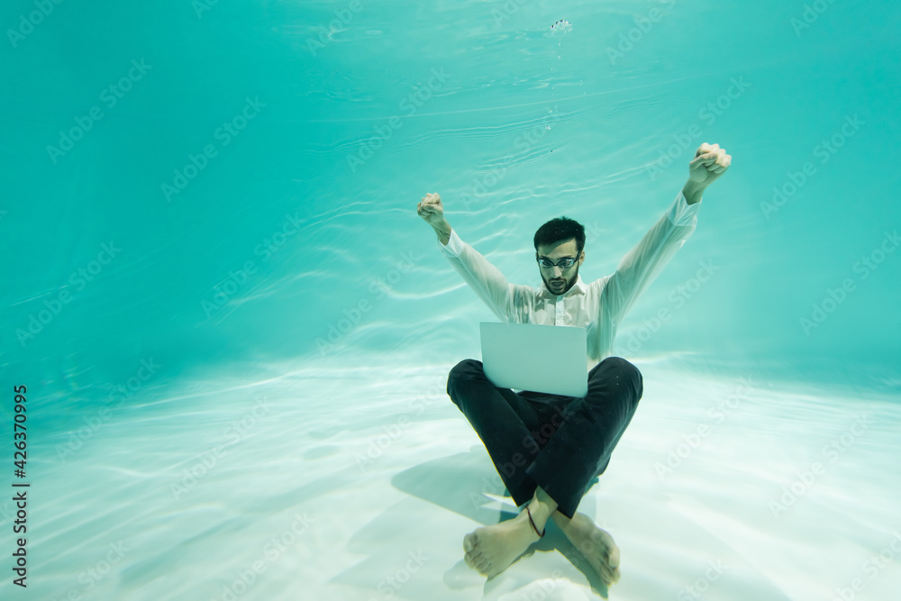 Muslim businessman showing yeah gesture near laptop underwater