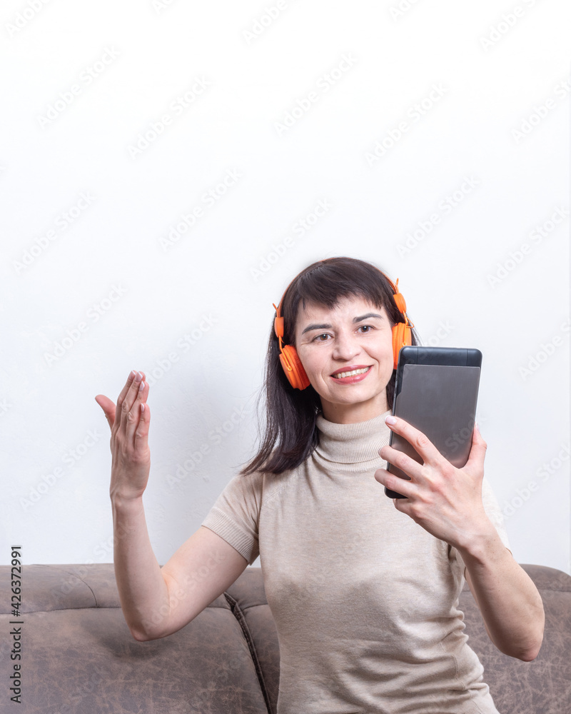 Charming brunette woman sitting on sofa wearing orange headphones having video call and gesturing Charming brunette woman sitting on sofa wearing orange headphones having video call and gesturing