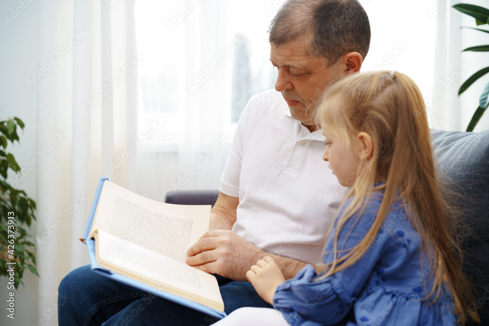 Grandfather reading a book to his little graddaughter in living room Grandfather reading a book to his little graddaughter in living room