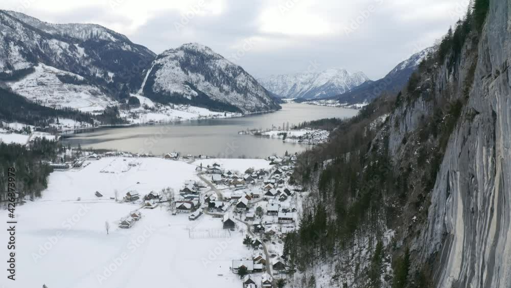 Aerial view moving shot, Scenic view of a town near the hill of Lake grundlsee in Styria, Austria, mountain range and cloudy sky in background. Aerial view moving shot, Scenic view of a town near the hill of Lake grundlsee in Styria, Austria, mountain range and cloudy sky in background.